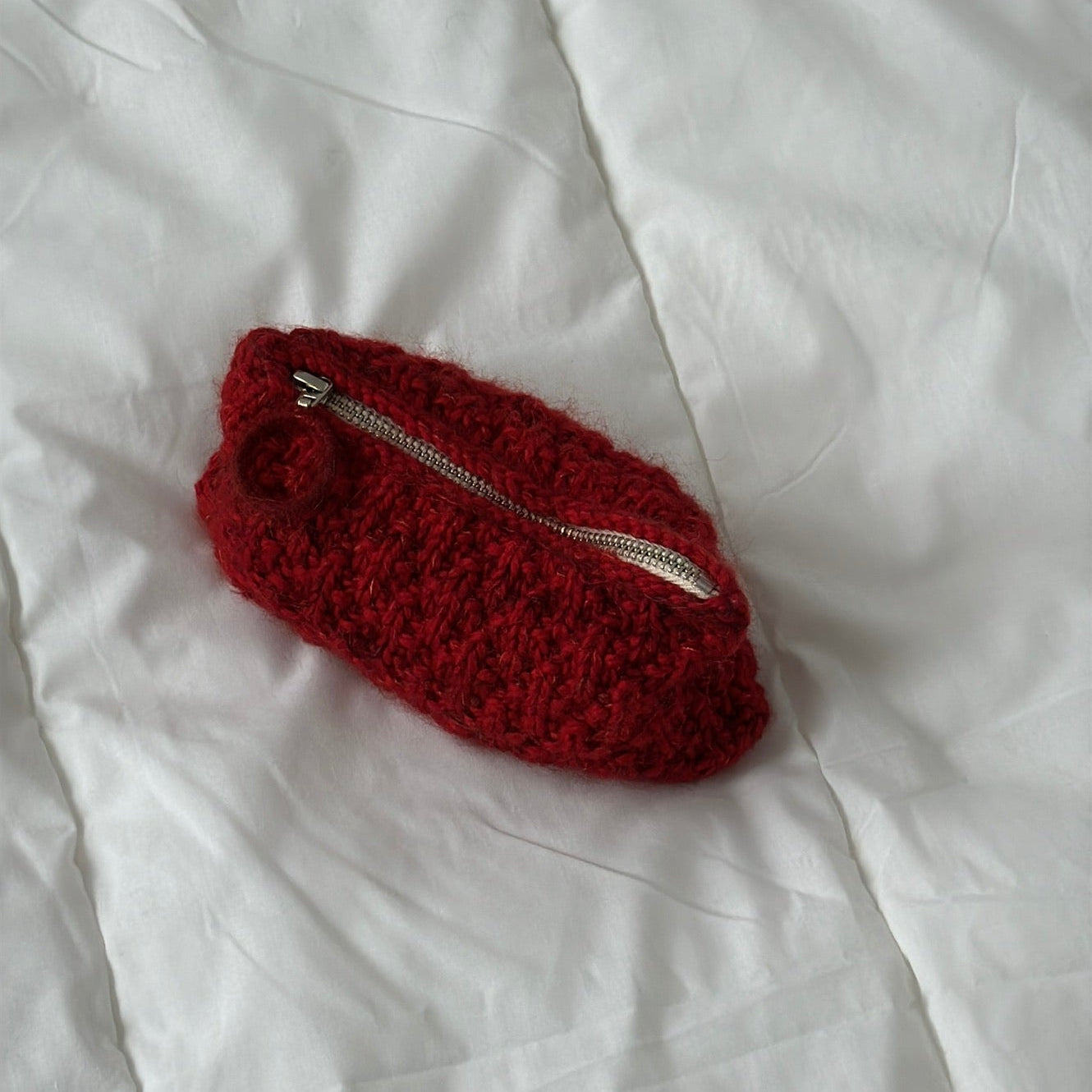 Red textured pouch with a silver zipper on a white fabric background
